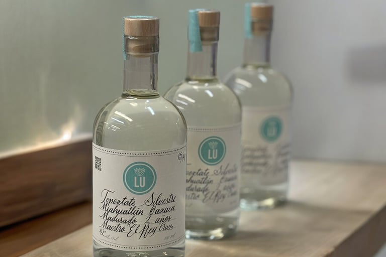 Botellas de Lu Mezcal con fondo blanco en una mesa de madera