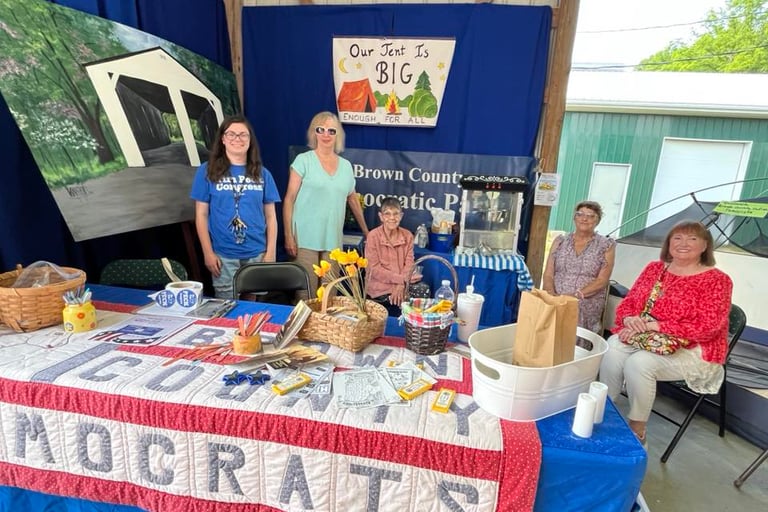 Five women sit or stand behind the Democrats booth at the fair