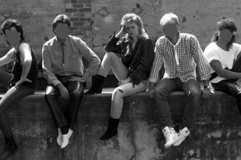 Black and white image of a young woman sitting on a wall with her four male band mates 