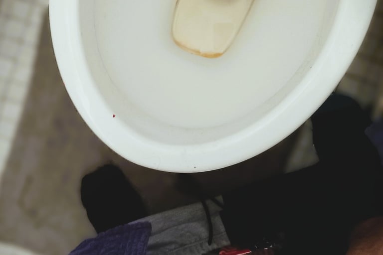 a male holding his penis over a toilet bowl on white tiles