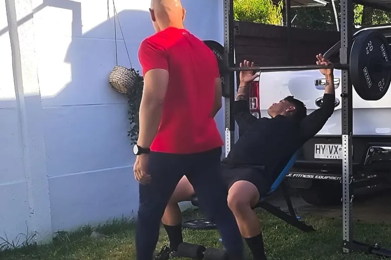 Cliente Carlos en press de banca supervisado por su personal trainer en Santiago.