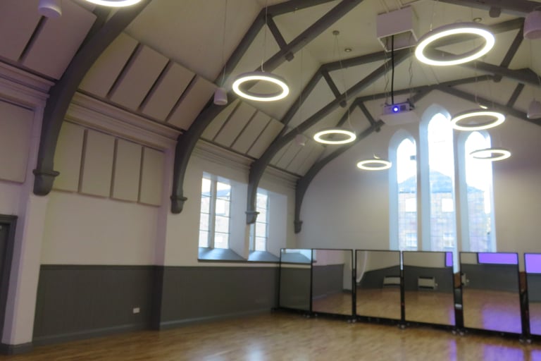A large well-lit hall with a vaulted ceiling and large windows. It has a flat wood floor.