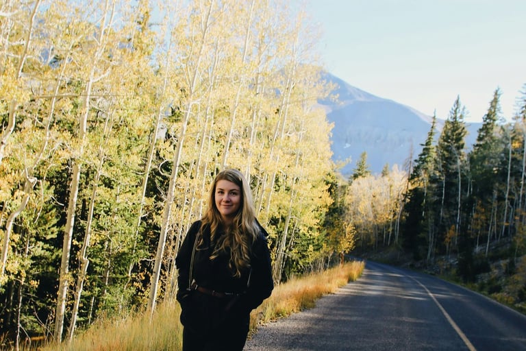 lady walking on a road with a forest and mountains in the backgroun