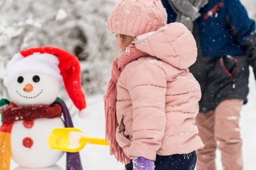 a young child standing in the snow with a snowman