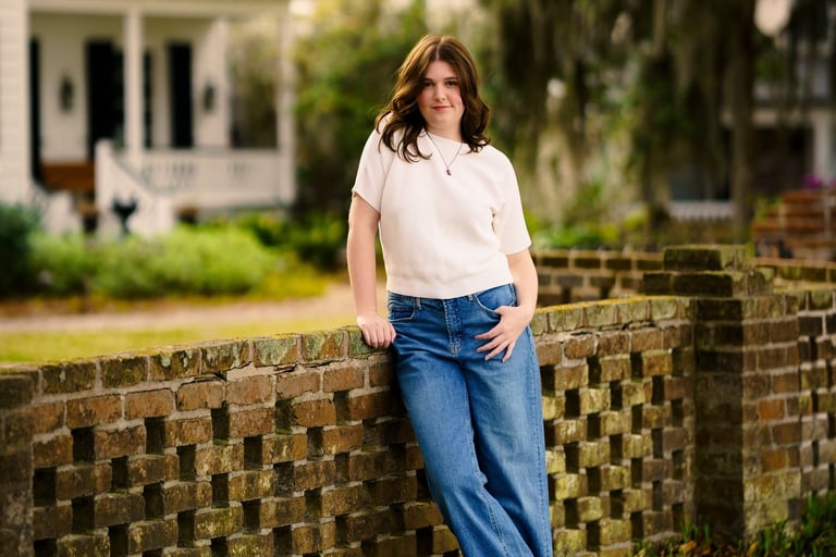 professional portrait of a woman leaning against a brick wall with a house behind her