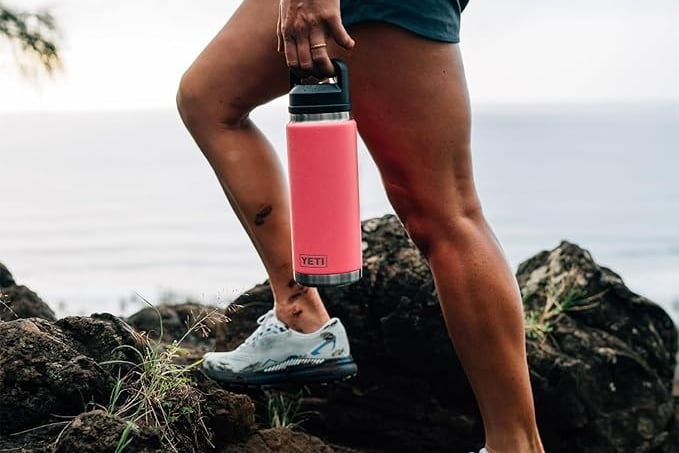 Pink YETI Rambler bottle filled with ice water at the beach.