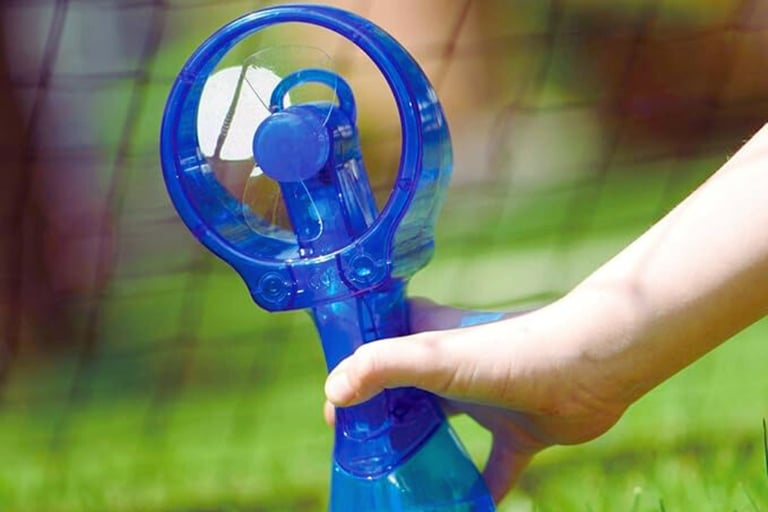 Handheld misting fan spraying water on sunny day