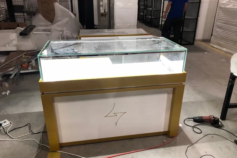 Custom lighted glass jewelry display case with gold trim in a retail manufacturing warehouse.