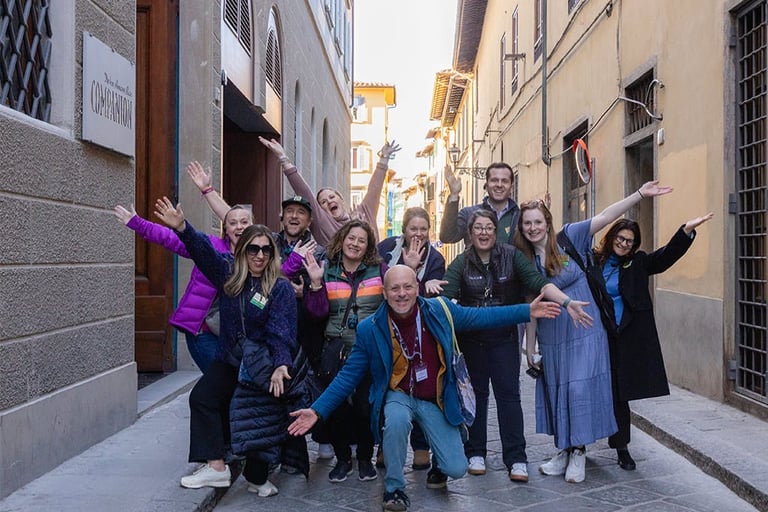 A cheerful group of tourists posing on a narrow historic street during a guided walking tour in Florence, Italy.
