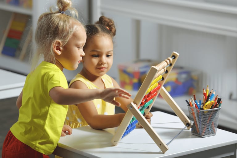 Two young girls learning math using a wooden abacus with colorful beads in a classroom.