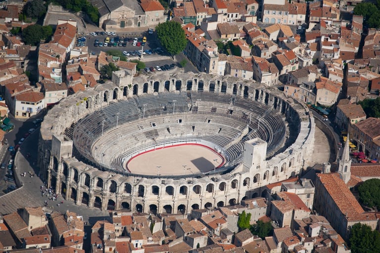 Aerial view of the ancient Roman amphitheater Arles Arena in France surrounded by historic red-roofed buildings.