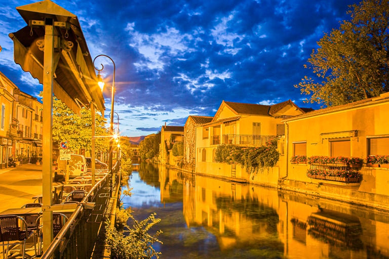 Scenic night view of a canal in L'Isle-sur-la-Sorgue, France, with yellow buildings reflecting in the water.