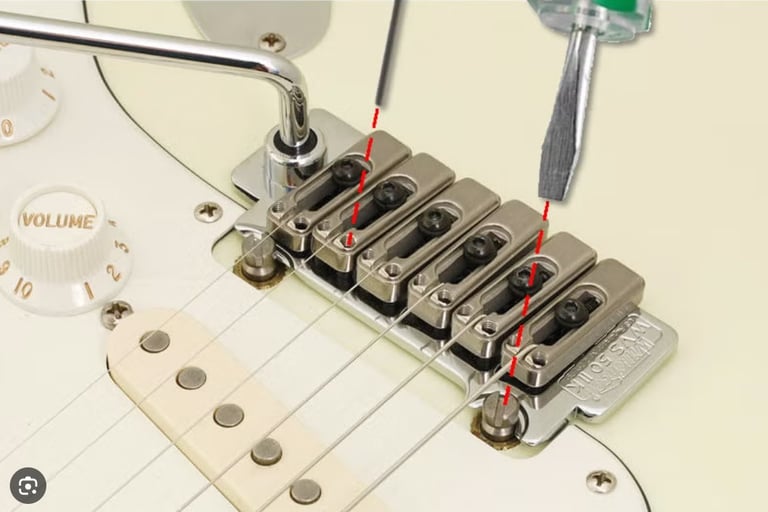 A person using a screwdriver to adjust the intonation on an electric guitar bridge system.