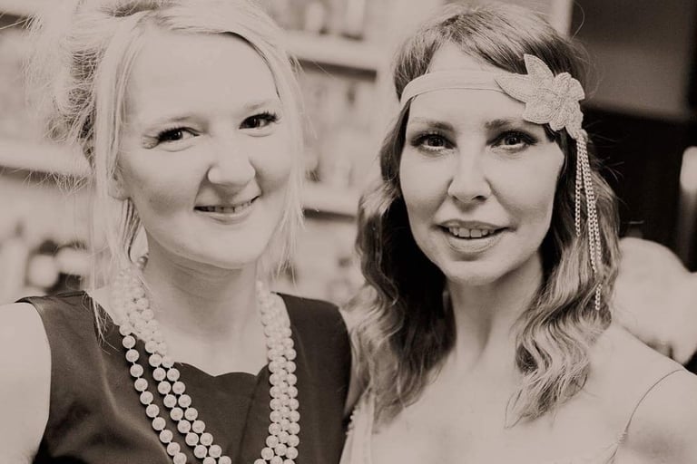 two girls dressed in 1920s costume are smiling at a themed murder mystery party.