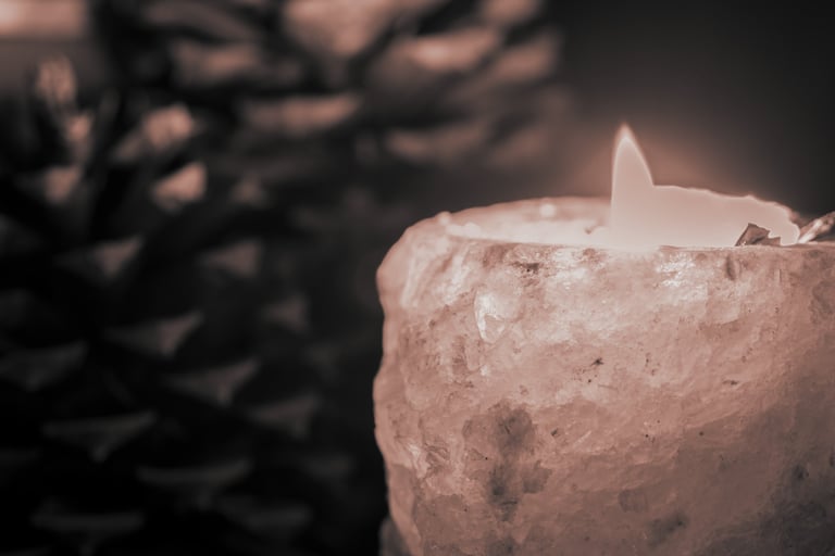 Close-up of a lit candle in a crystal holder with blurred pinecone in background
