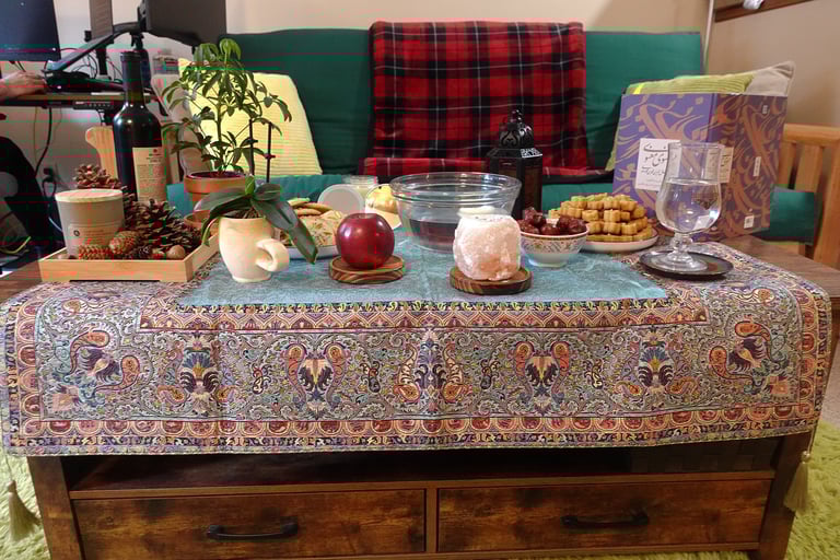 Haft-seen table with candles, apple, dates, cookies, book, and plants on a coffee table
