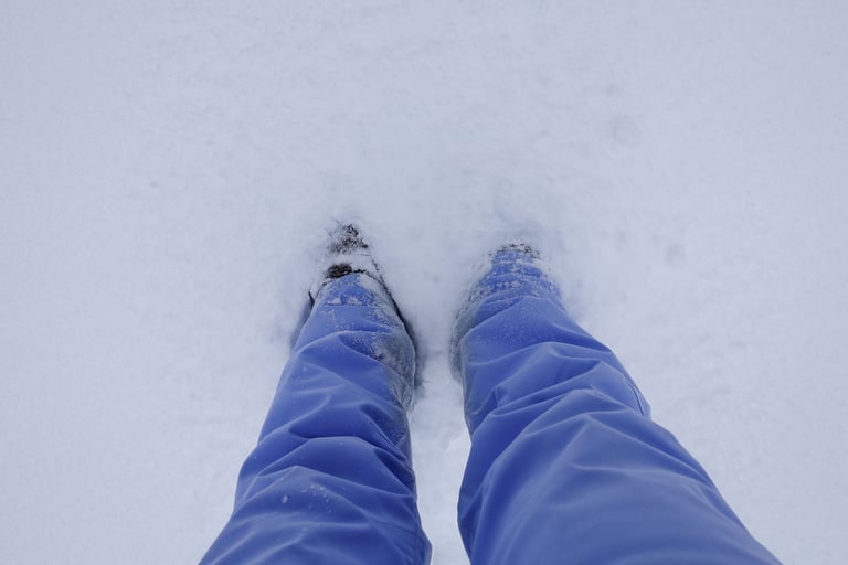 Person standing in deep snow, looking down at their legs and boots partially covered by snow.