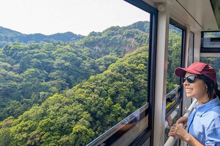 Woman smiling from a cable car descending toward a quiet village surrounded by lush green hills in Shizuoka, Japan.