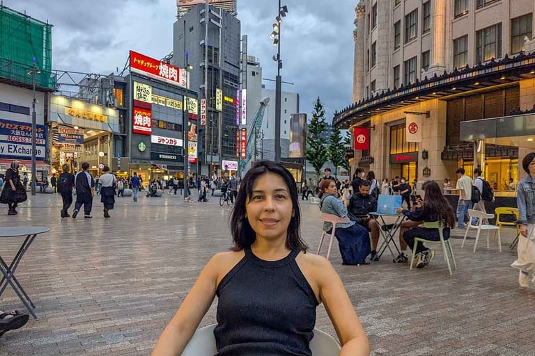 Woman sitting in a public square in downtown Osaka as evening crowds gather around the city center.