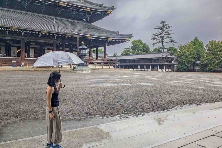 Woman holding an umbrella in the courtyard of Nishi Hongan-ji Temple during a rainy afternoon in Kyoto, Japan.