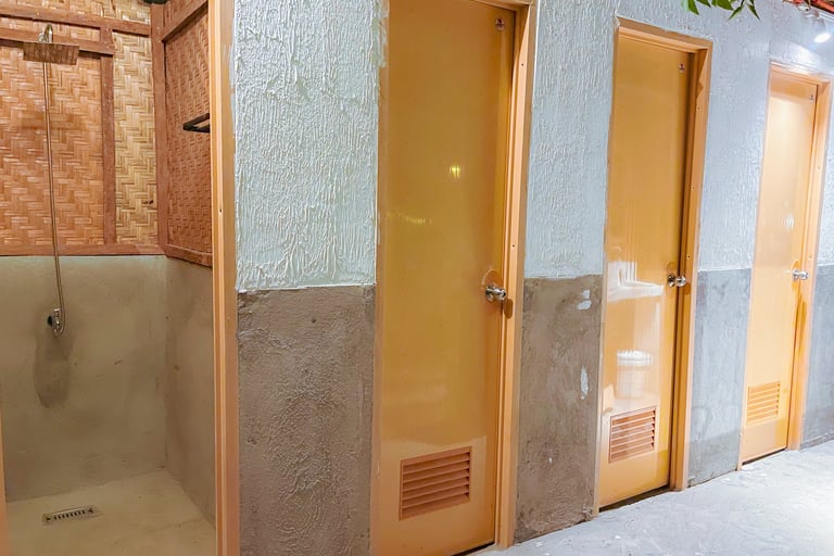 Rustic bathroom facility with bamboo shower stall and row of private wooden toilet doors.