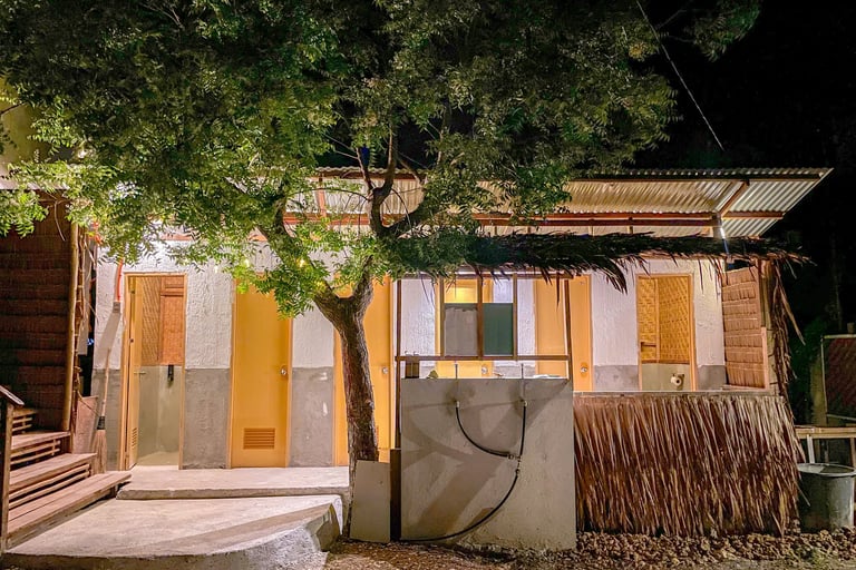 Rustic tropical bungalow at night with bamboo walls, thatched roof, and warm exterior lighting.