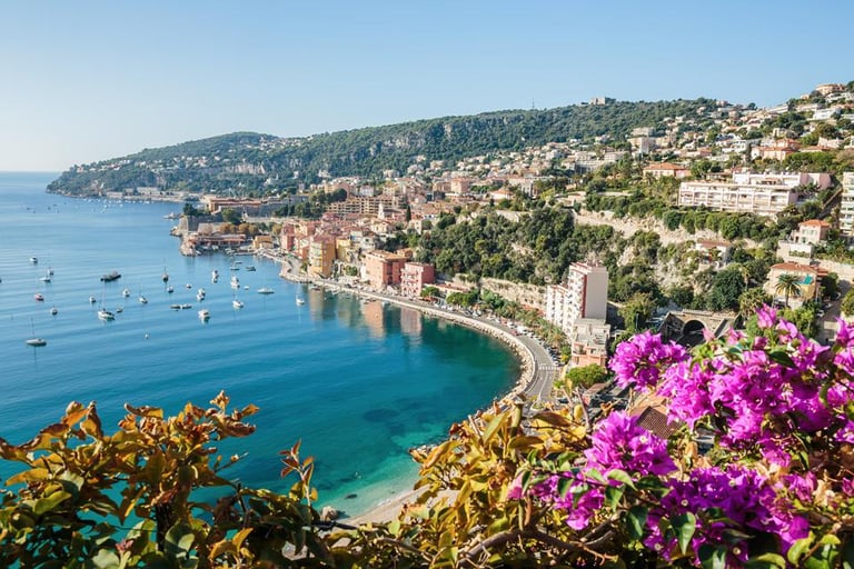 Scenic view of Villefranche-sur-Mer bay on the French Riviera with colorful buildings, turquoise water, and purple flowers.