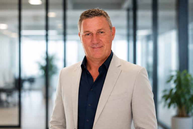 Professional portrait of a middle-aged male executive in a light gray suit jacket inside a modern office.