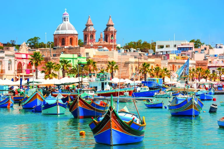 Colorful traditional Luzzu boats floating in Marsaxlokk harbor with the historic parish church in Malta.