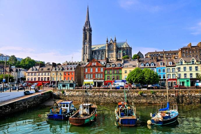 Fishing boats in Cobh harbor with colorful houses and St. Colman's Cathedral in Ireland.