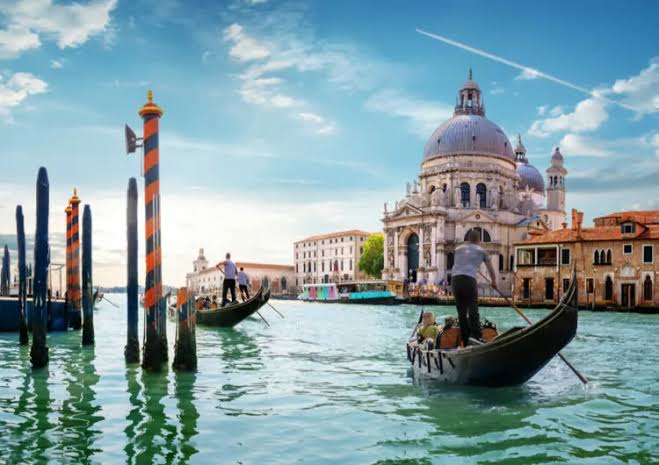 Gondolas cruising the Grand Canal past the historic Santa Maria della Salute basilica in Venice, Italy.
