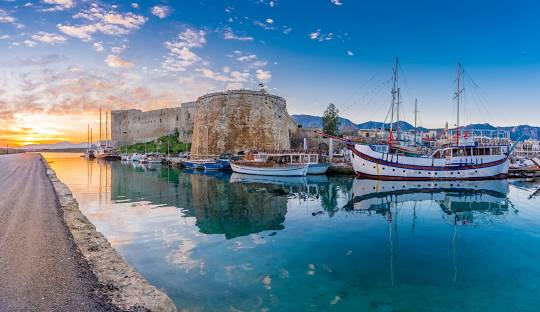 Kyrenia Harbour in Northern Cyprus featuring the historic castle and sailboats at sunset.