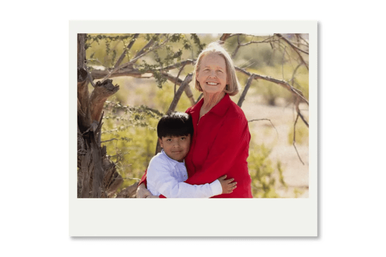 Smiling grandmother and grandson hugging outdoors in a sunny park landscape.