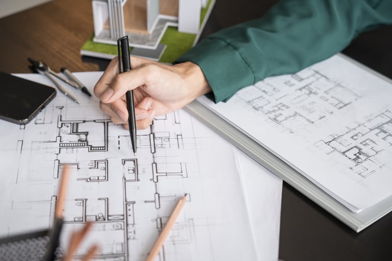 Architect sketching on a detailed house floor plan blueprint with a pen at a wooden desk.