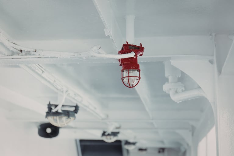 Industrial red marine cage light mounted on a white ship deck ceiling.