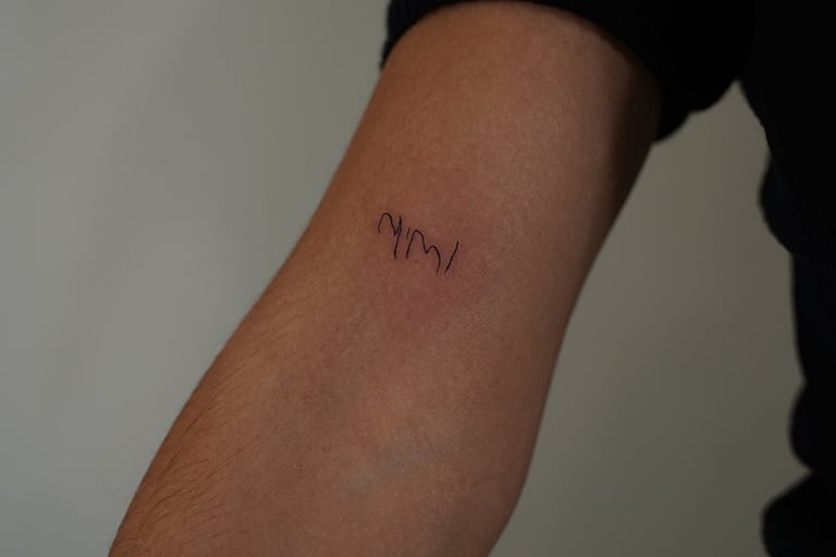 Tatuaje fineline en Madrid con lettering mimi en trazo manuscrito ultrafino en el antebrazo