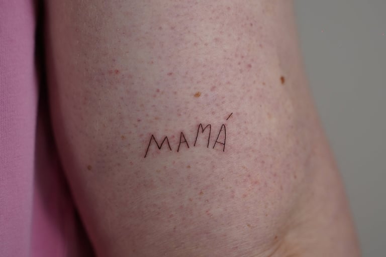 Tatuaje fineline en Madrid con lettering MAMÁ en mayúsculas trazo fino en el brazo