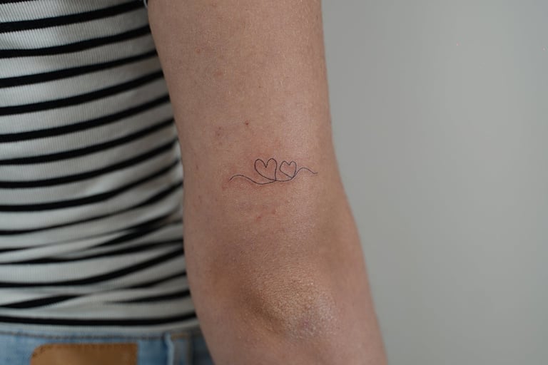 Tatuaje fineline en Madrid de dos corazones pequeños unidos por línea continua en el brazo