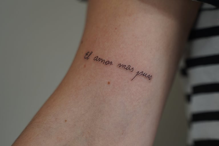 Tatuaje fineline en Madrid con frase el amor más puro en cursiva fina en el antebrazo