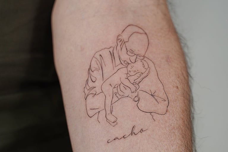 Tatuaje fineline en Madrid de figura masculina abrazando a un bebe con lettering 