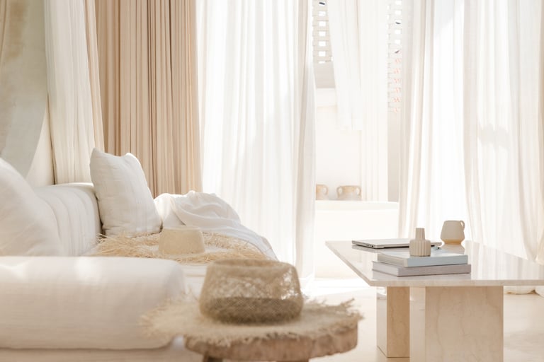 Linen curtains filtering direct midday light onto a plaster wall.