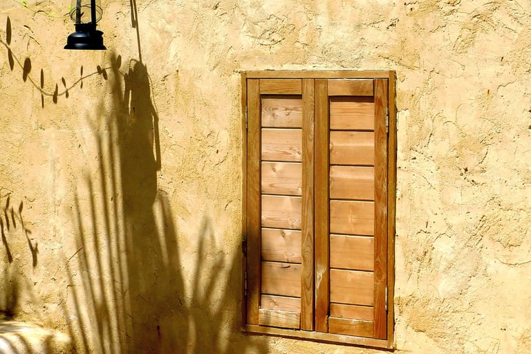 Slim timber window with shutters set into a thick Mediterranean stone wall.
