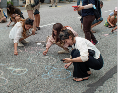 Children drawing and learning on the ground during an outdoor creative activity.