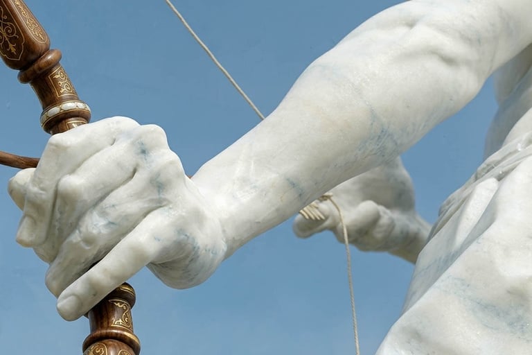 Close-up of a marble statue's hand gripping a wooden bow against a clear blue sky.