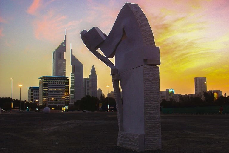 A stone sculpture stands against the Dubai skyline and Emirates Towers during a vibrant sunset.