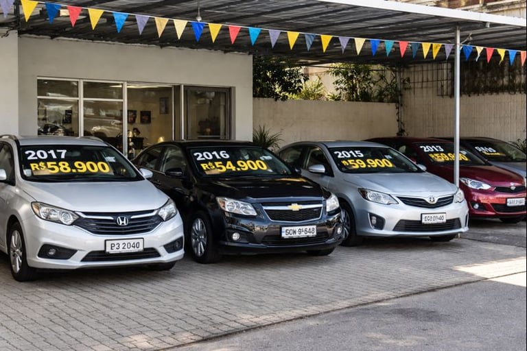 Pátio de loja de carros usados com veículos à venda, placas de preço e ano em português, sem pessoas