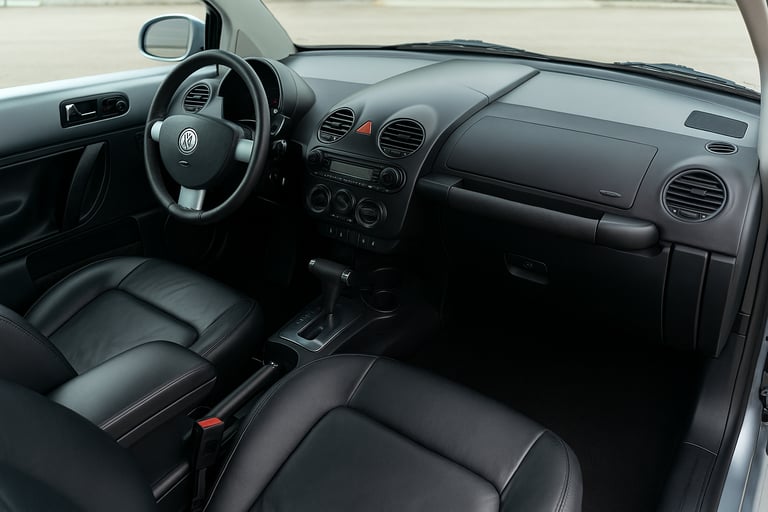 Interior do Volkswagen New Beetle com painel, volante e bancos em couro preto.