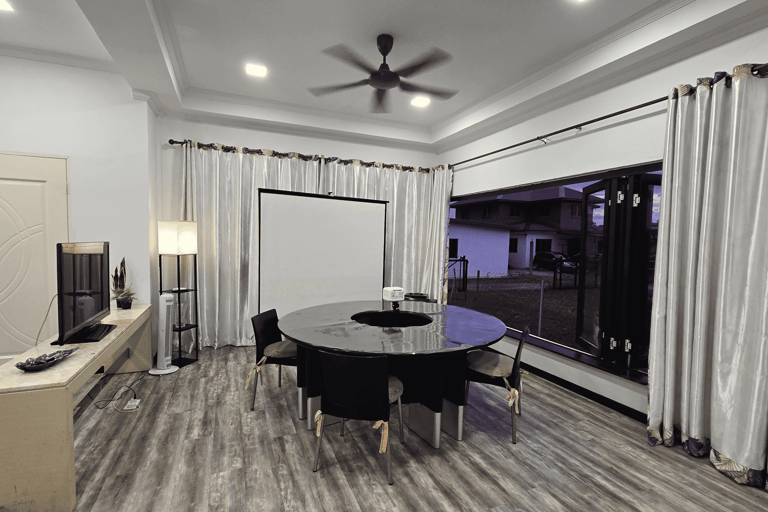 Modern conference room with a round black table, projector screen, and large windows with silver curtains.