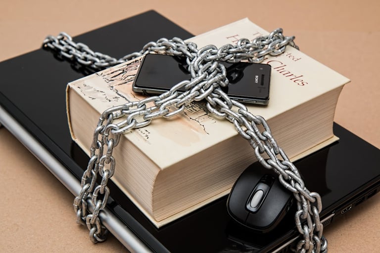 a closed laptop with a, book on top of it, and a cell phone all secured by a large chain and lock