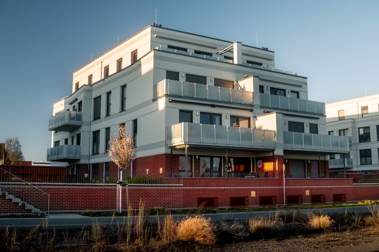 Mehrfamilienhaus mit roten Klinkersteinen im Erdgeschoss und weißen Fassaden mit Balkonen 